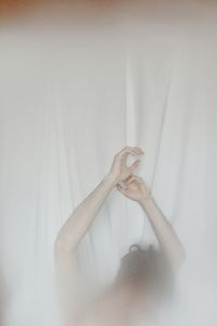 Woman with arms raised against curtain