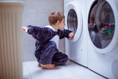 Full length of boy sitting by washing machine