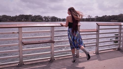 Full length of woman standing on railing against sky