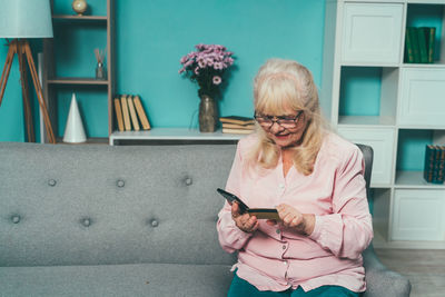 Cheerful grandmother using mobile phone while sitting on sofa