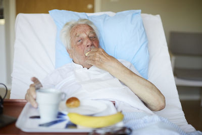 Senior man eating breakfast on bed in hospital ward