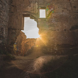 Sunlight streaming through arch on wall against sky during sunset