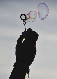 Low angle view of hand holding bubbles against sky