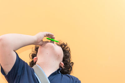 Close-up of boy placing fidget spinner on nose against yellow background