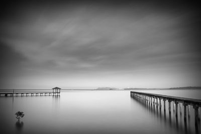 Pier over river against cloudy sky