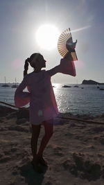Full length of young woman holding hand fan at beach against sky