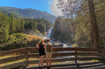 People standing by railing against trees and mountains