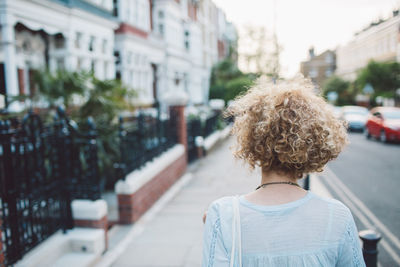 Rear view of mid adult woman standing on footpath in city