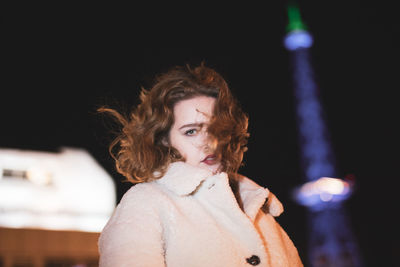 Portrait of beautiful young woman standing against illuminated light at night