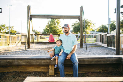 Father and son looking away while sitting at playground