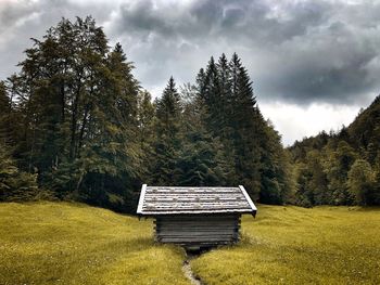 Empty bench on field by trees against sky