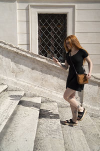 Red hair girl walking up the stairs looking at the phone in sunny day