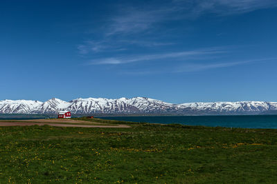 Seascape amidst green field and snowcapped mountain