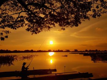 Silhouette tree by lake against sky during sunset