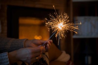Midsection of woman holding illuminated sparklers at home