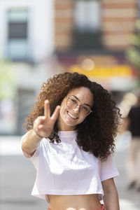 Smiling woman making peace sign during sunny day