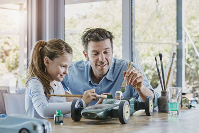 Father and daughter painting a toy race car