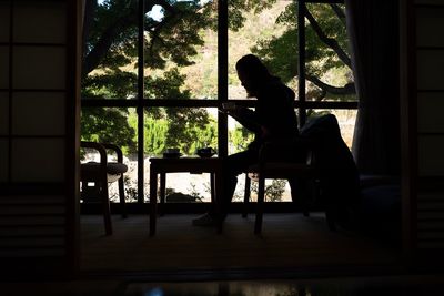 Side view of silhouette woman sitting by window