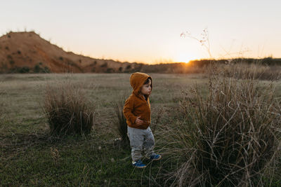 Cute boy standing on field during sunset