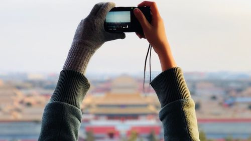 Cropped hands of woman photographing with camera against sky