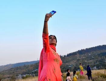 Woman photographing with mobile phone against sky