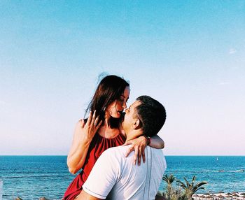 Couple kissing at beach against sky