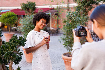 Friend photographing teenage girl through camera while standing on street