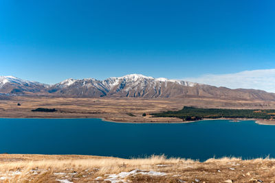 Scenic view of lake by mountains against clear blue sky