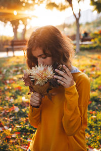 Curly young girl in yellow sweater on the grass with autumn bouquet of dry leaves and flowers