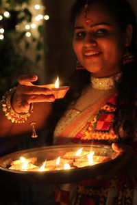 Portrait of woman holding illuminated diya at night