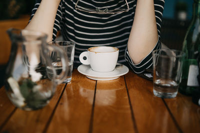 Midsection of woman with coffee cup on table