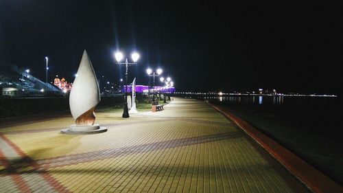 Illuminated walkway by river against sky at night