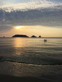 Silhouette people standing on shore by sea against sky during sunset