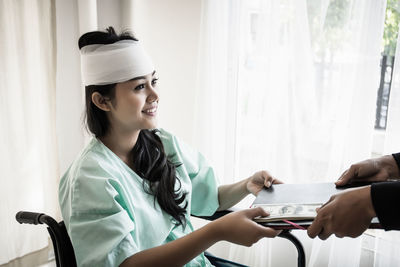 Smiling woman with physical injury giving money to doctor