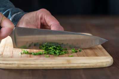 A chef's hands chopping fresh chives on a wooden cutting board.