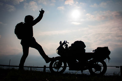 Silhouette men with bicycle against sky during sunset