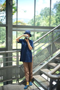 Full length of woman photographing through camera while standing by railing