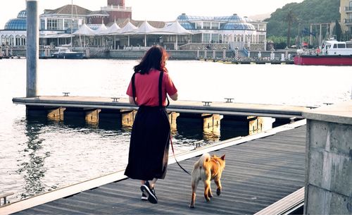 Rear view of woman with dog walking on pier by lake