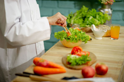 Midsection of chef preparing salad in bowl