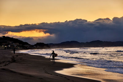 Silhouette people on beach against sky during sunrise