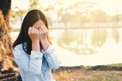 Woman covering face with fists by lake