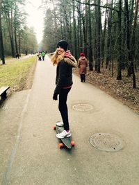 Portrait of happy woman standing on skateboard amidst trees