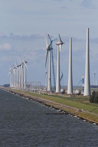 Windmills at riverbank against sky