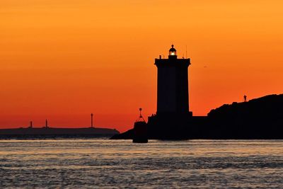 Silhouette lighthouse at sea against sky during sunset