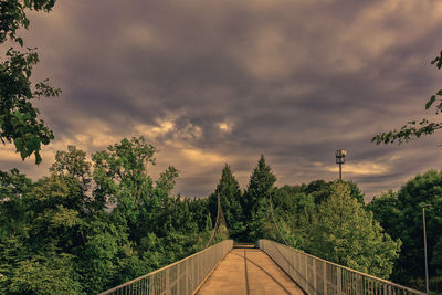 Footbridge amidst trees against sky during sunset