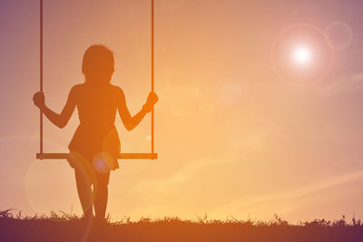 Silhouette girl swinging against sky during sunset