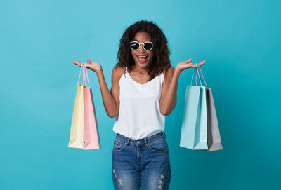 Portrait of happy woman holding shopping bags while standing against turquoise background