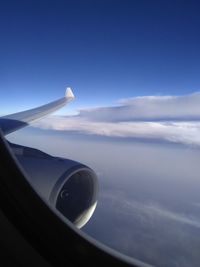 Cropped image of airplane flying over cloudscape against blue sky