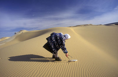 Side view of man picking up plastic bottle on desert