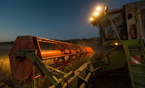 Illuminated machine harvesting crops on field at dusk